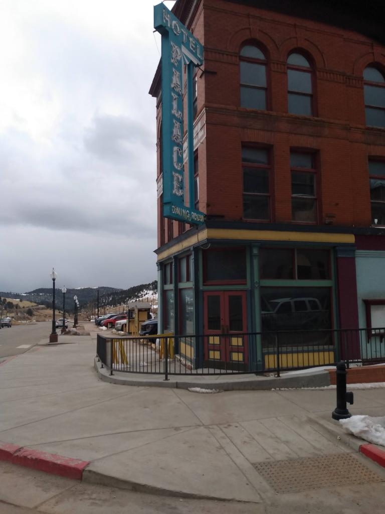 Corner of building bearing sign proclaiming "Palace Hotel" and corner entrance, wood and glass four section doors.