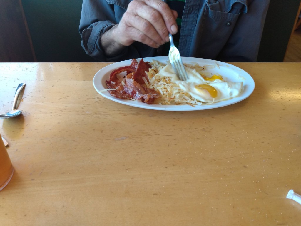 A pjoto of a plate of bacon and eggs and friend potatoes.