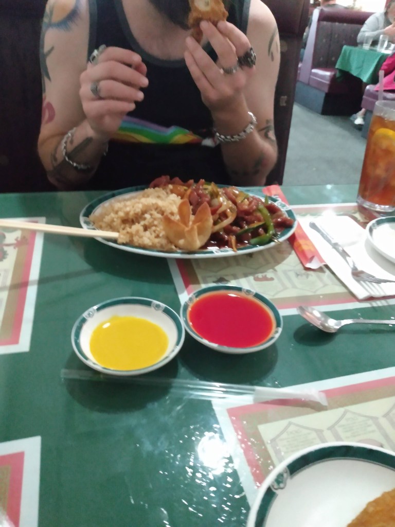 Photo of two bowls with orange sweet and sour sauce and yellow hot mustard, with a person eating a Chinese dinner in the background.