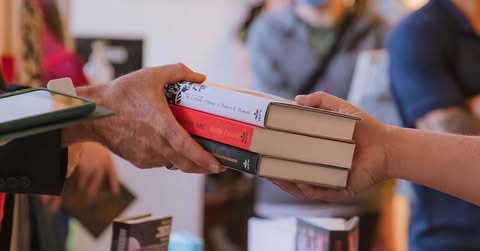 A stack of three books being passed between two hands.