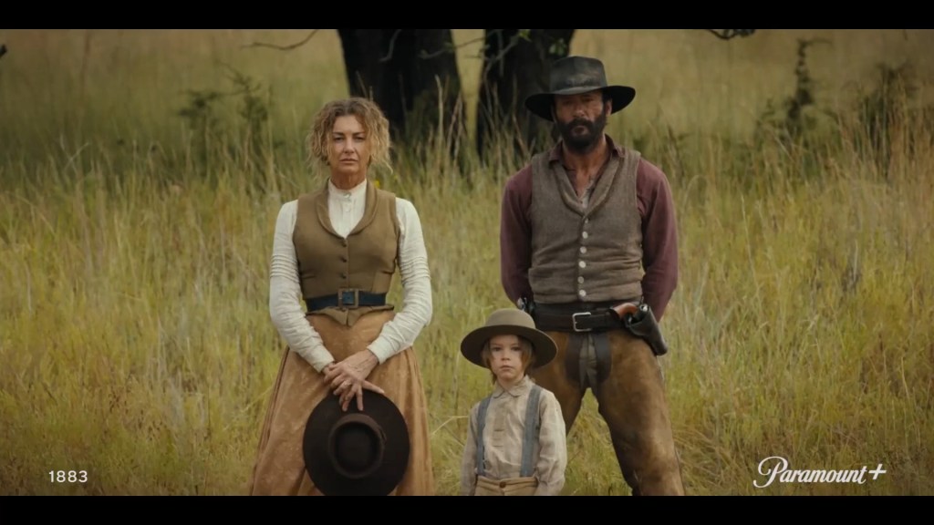 A woman, a man, and a small boy standing in tall grasses in western garb.