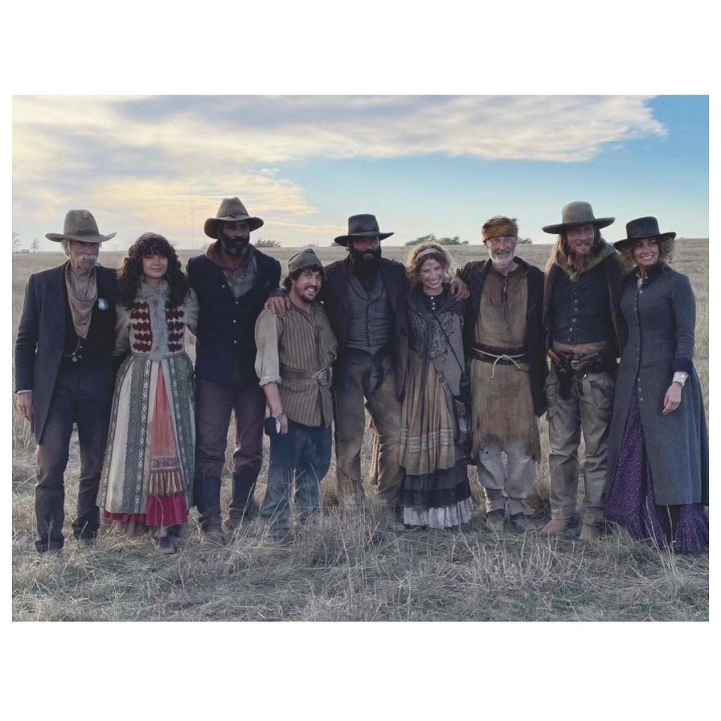 A group of people in western garb stand together in a line with smiles on their faces.