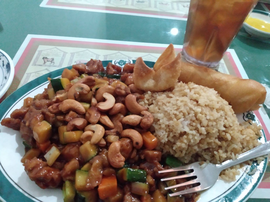 Cashew chicken with fried rice, a wonton and a spring egg roll and a glass of golden brown iced tea