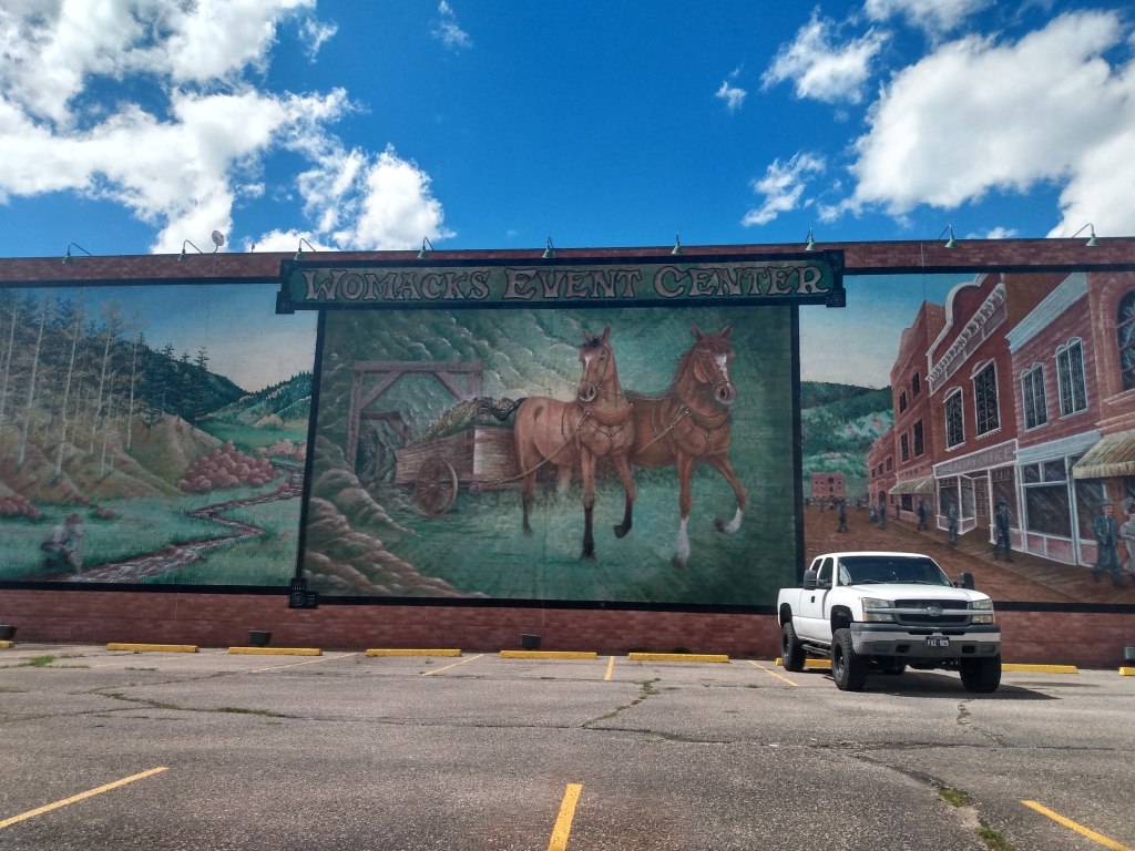 Three murals: one a mountain stream, one a horse drawn cart coming out of a mine, and the original buildings of Cripple Creek.